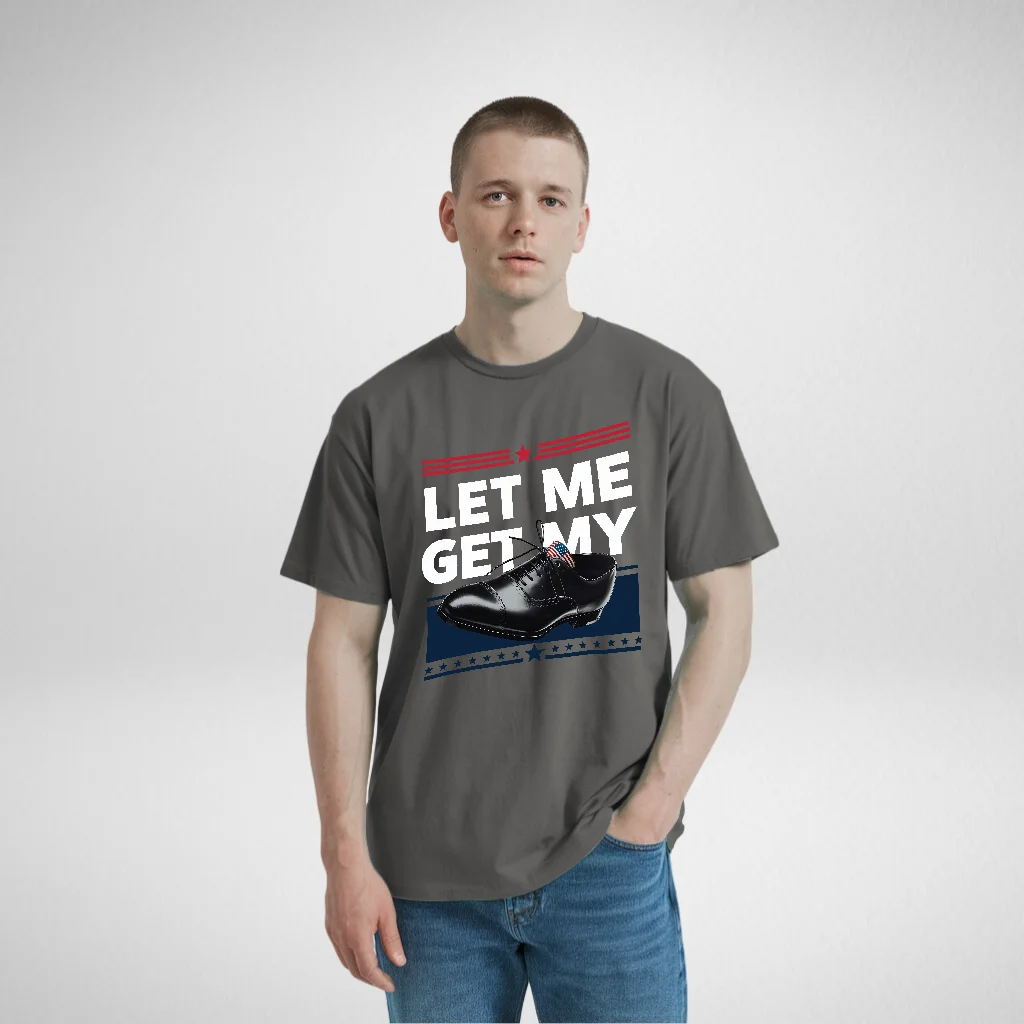 Man wearing a gray t-shirt with the bold text 'LET ME GET MY' and a polished black shoe illustration, standing casually with hands in his pockets.