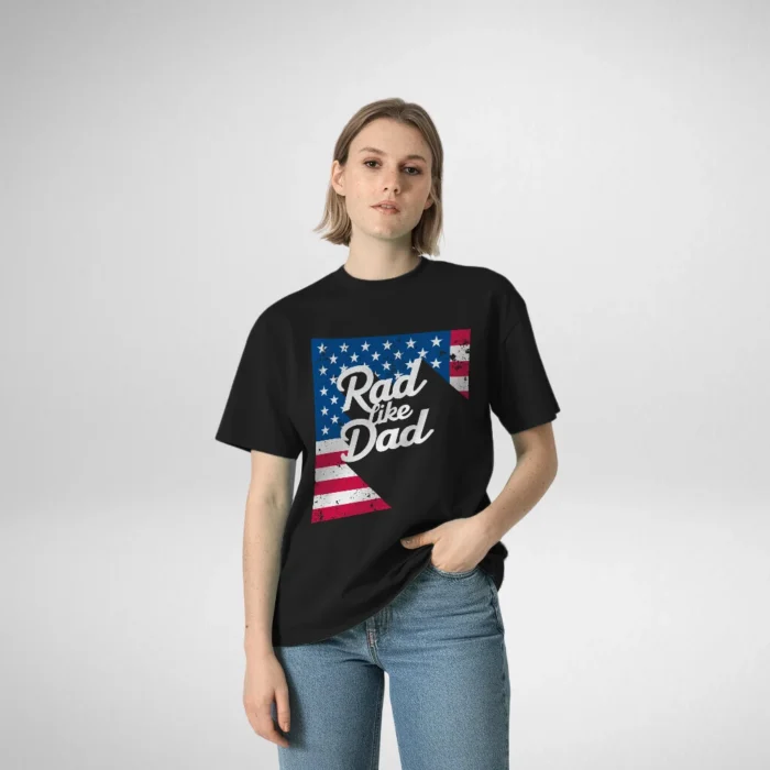 Woman modeling a black t-shirt featuring the text 'Rad Like Dad' with an American flag design, standing confidently with one hand in her pocket.